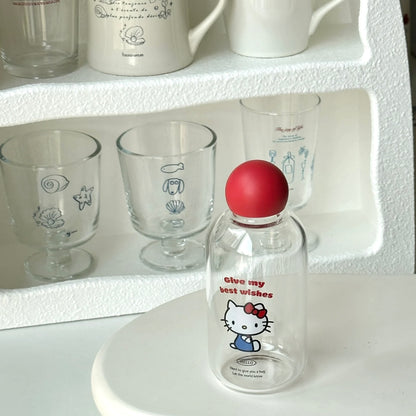 Clear bottle with cartoon character and red ball on a white surface with glasses in the background