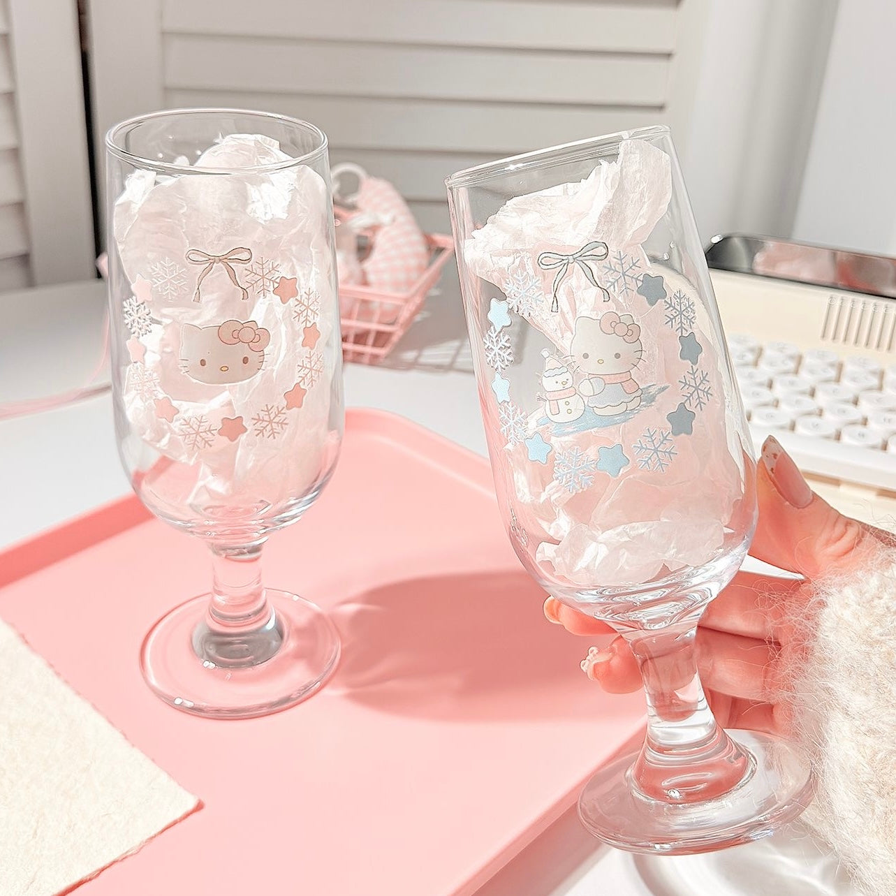 Two decorative glass goblets with cartoon character designs on a pink tray.