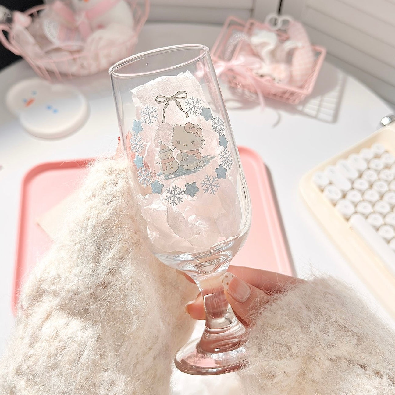 Glass with a Hello Kitty design held by a hand on a soft surface