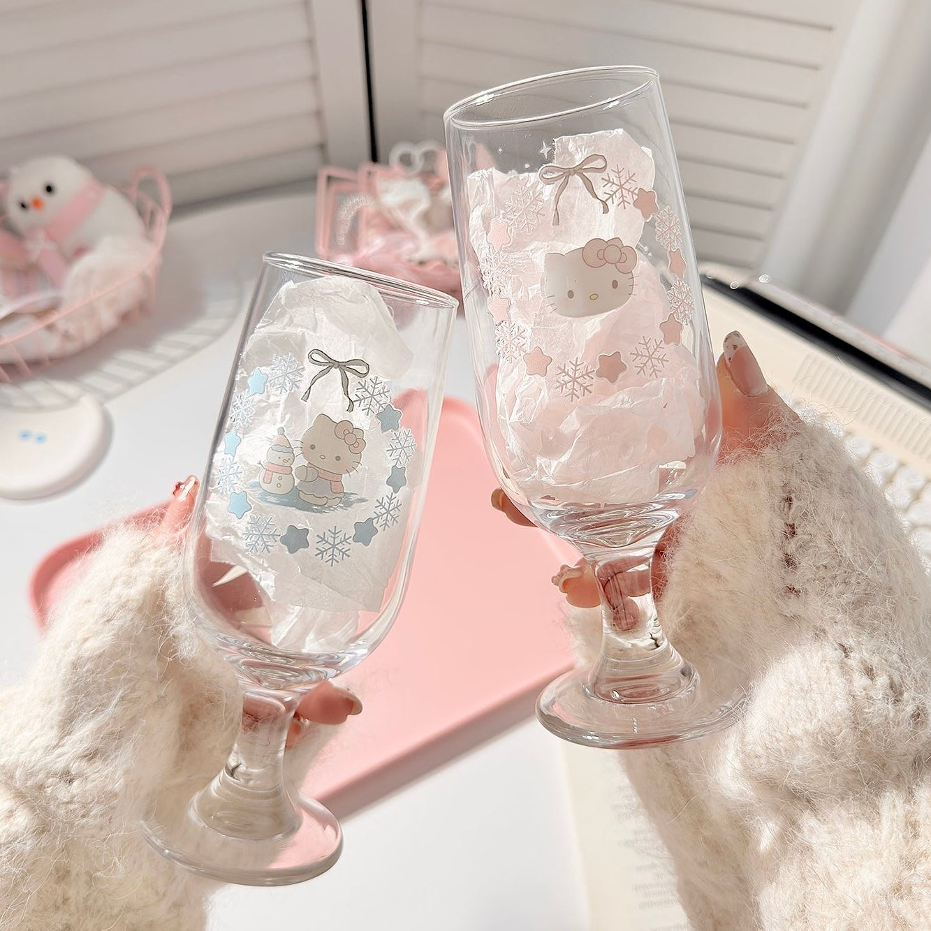 Two clear glasses with cartoon character designs held by a person wearing a white sweater.