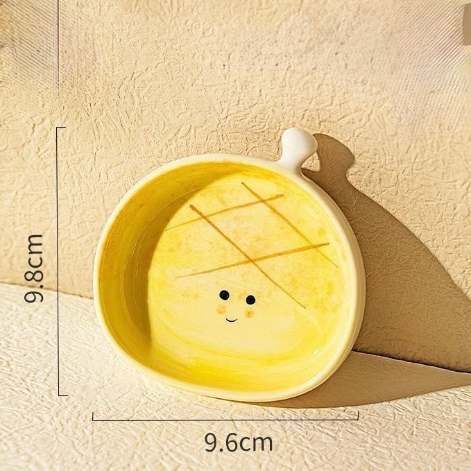 Yellow ceramic bowl with a face design on a beige background, showing measurements.