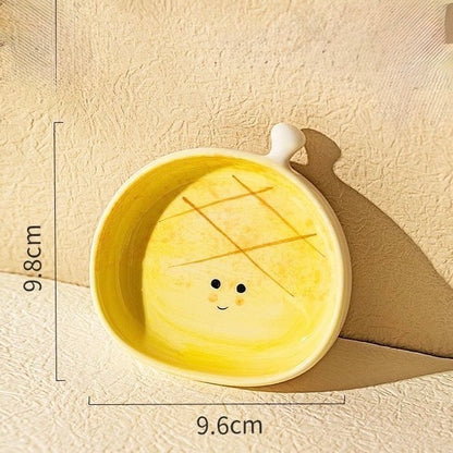 Yellow ceramic bowl with a face design on a beige background, showing measurements.