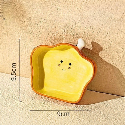 Yellow ceramic plate shaped like a slice of bread with a smiley face, placed on a textured beige surface.