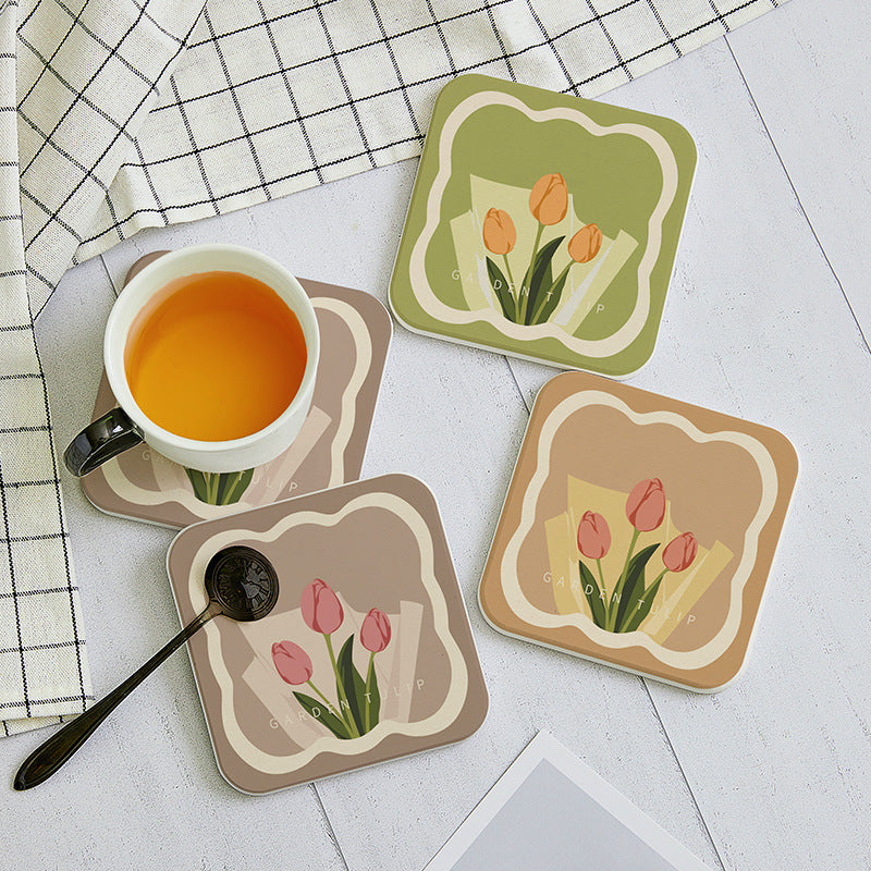 Set of four floral coasters with a cup of tea and spoon on a checkered tablecloth.