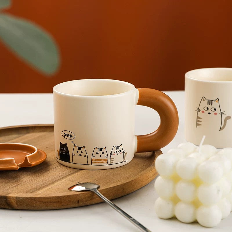 Ceramic mug with cat illustrations on a wooden tray with a candle and spoon.