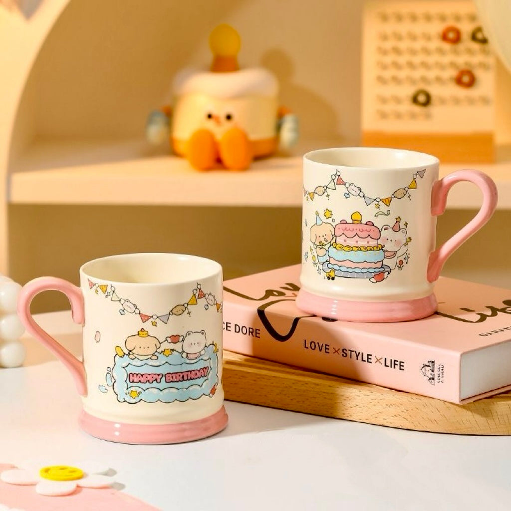 Two ceramic mugs with cartoon designs on a surface with a book in the background.