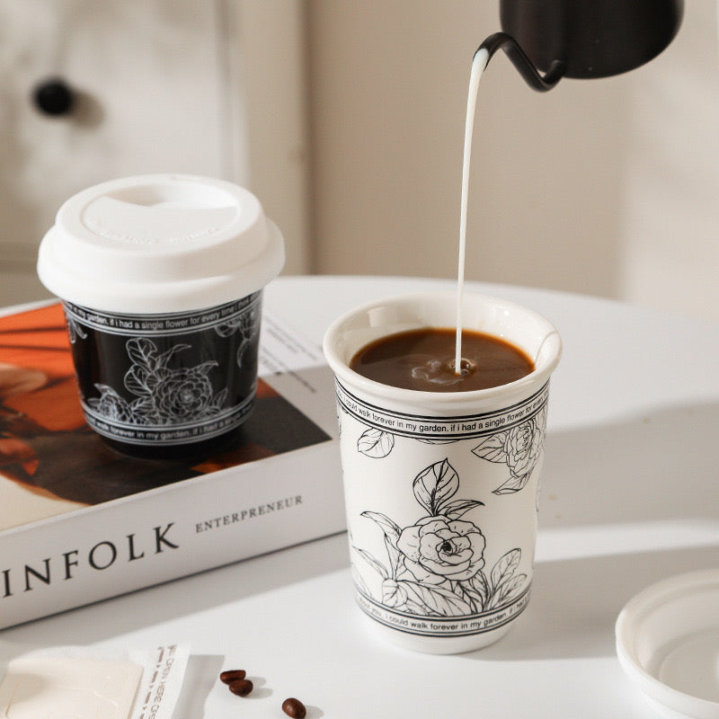 Coffee being poured into a white cup with black floral designs on a white surface.