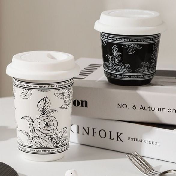 Two black and white floral-patterned coffee cups on a surface with books in the background.