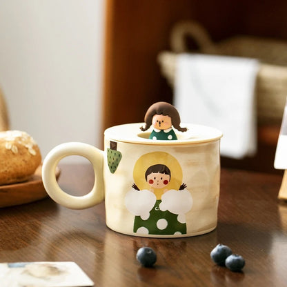 Two ceramic mugs with hand-drawn illustrations of cute couples, one wearing a green dress and the other in a black suit, displayed on a table.