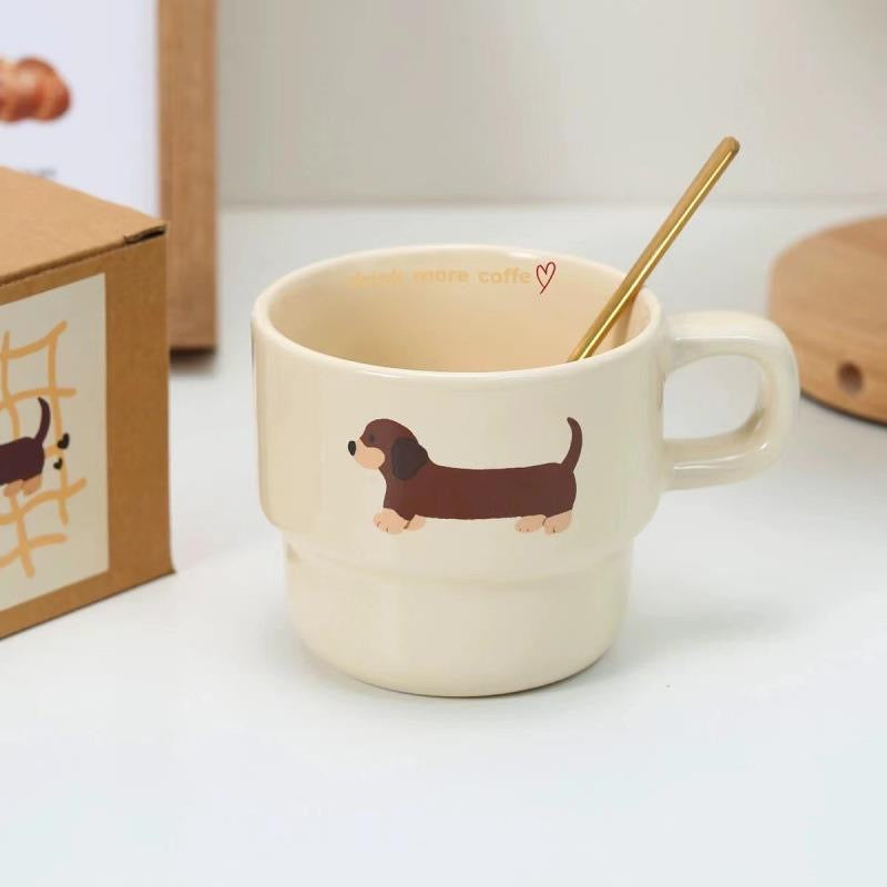 Two beige ceramic mugs with brown dachshund prints, stacked one inside the other, with a gift box visible in the background.