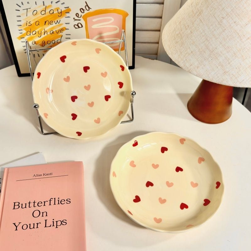 Two ceramic plates with heart patterns on a surface next to a book titled 'Butterflies On Your Lips'.