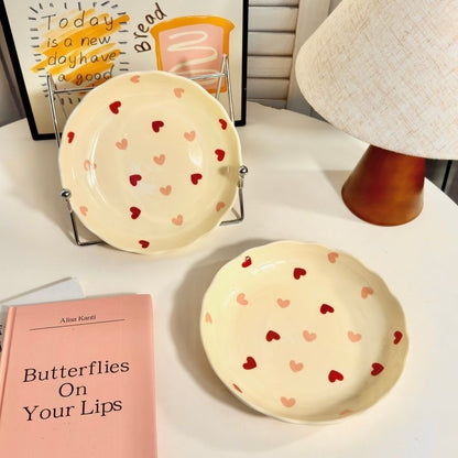 Two ceramic plates with heart patterns on a surface next to a book titled 'Butterflies On Your Lips'.