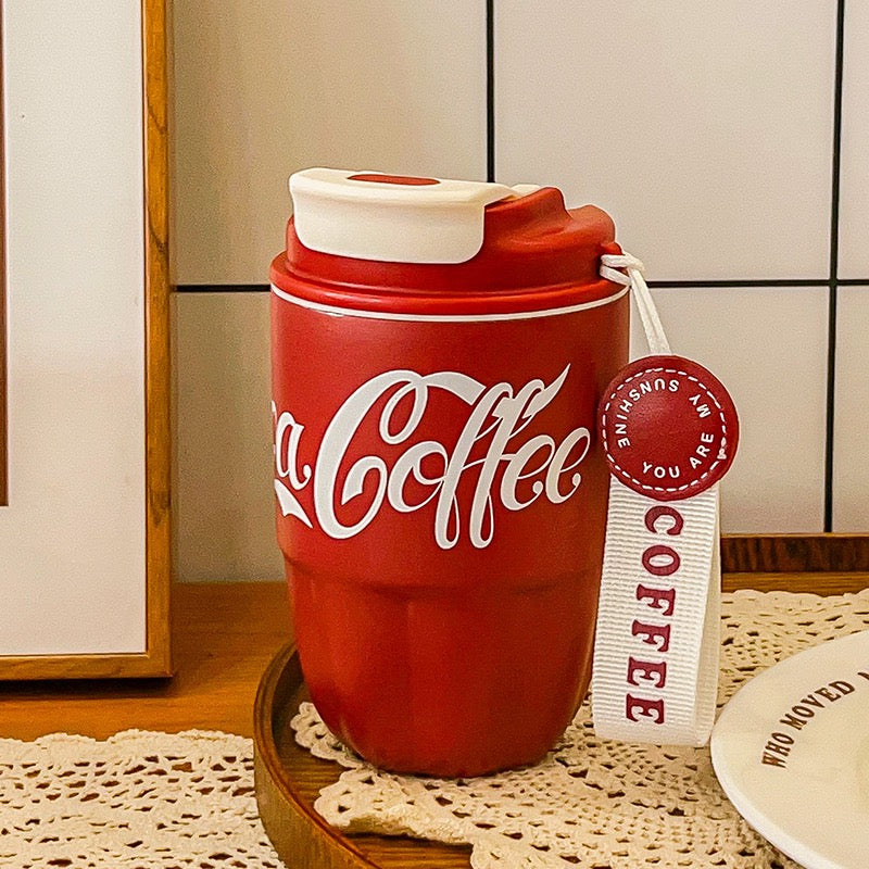 Two Coca Coffee Tumblers, one white and one red, with a 'Coca Coffee' print on them, being held in front of a Marshall speaker.